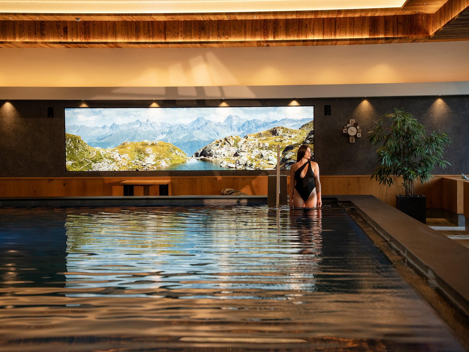 Bathing bliss at our hotel with pool in Serfaus Woman in black swimsuit standing in indoor pool with mountain view window