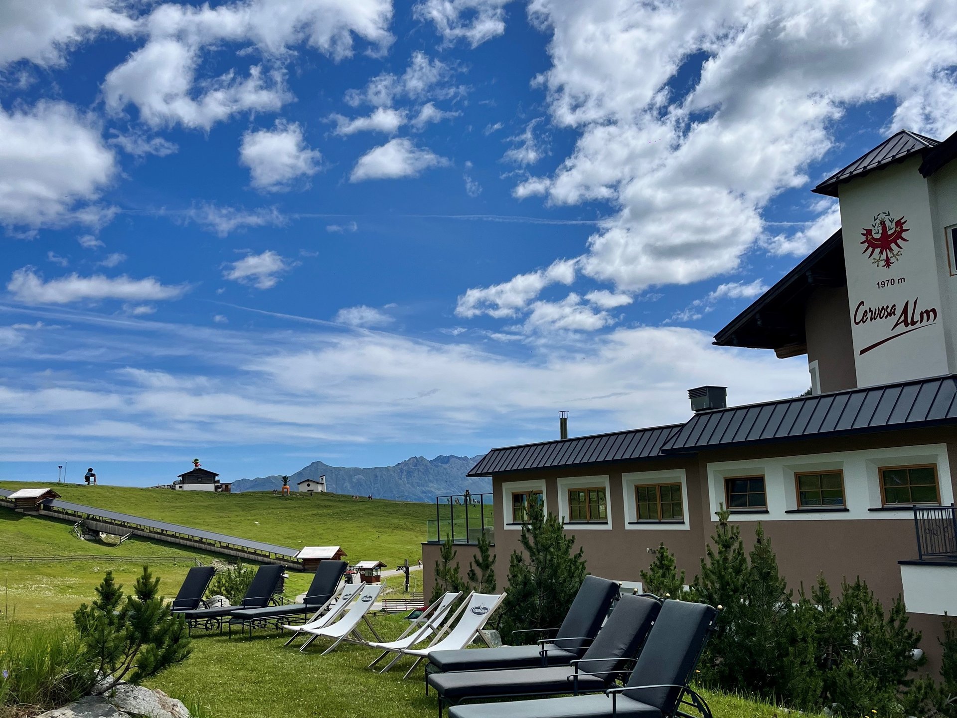 Die Cervosa Alm auf 2 000 Metern Liegestühle auf grüner Wiese vor Berggasthof unter blauem Himmel mit Wolken