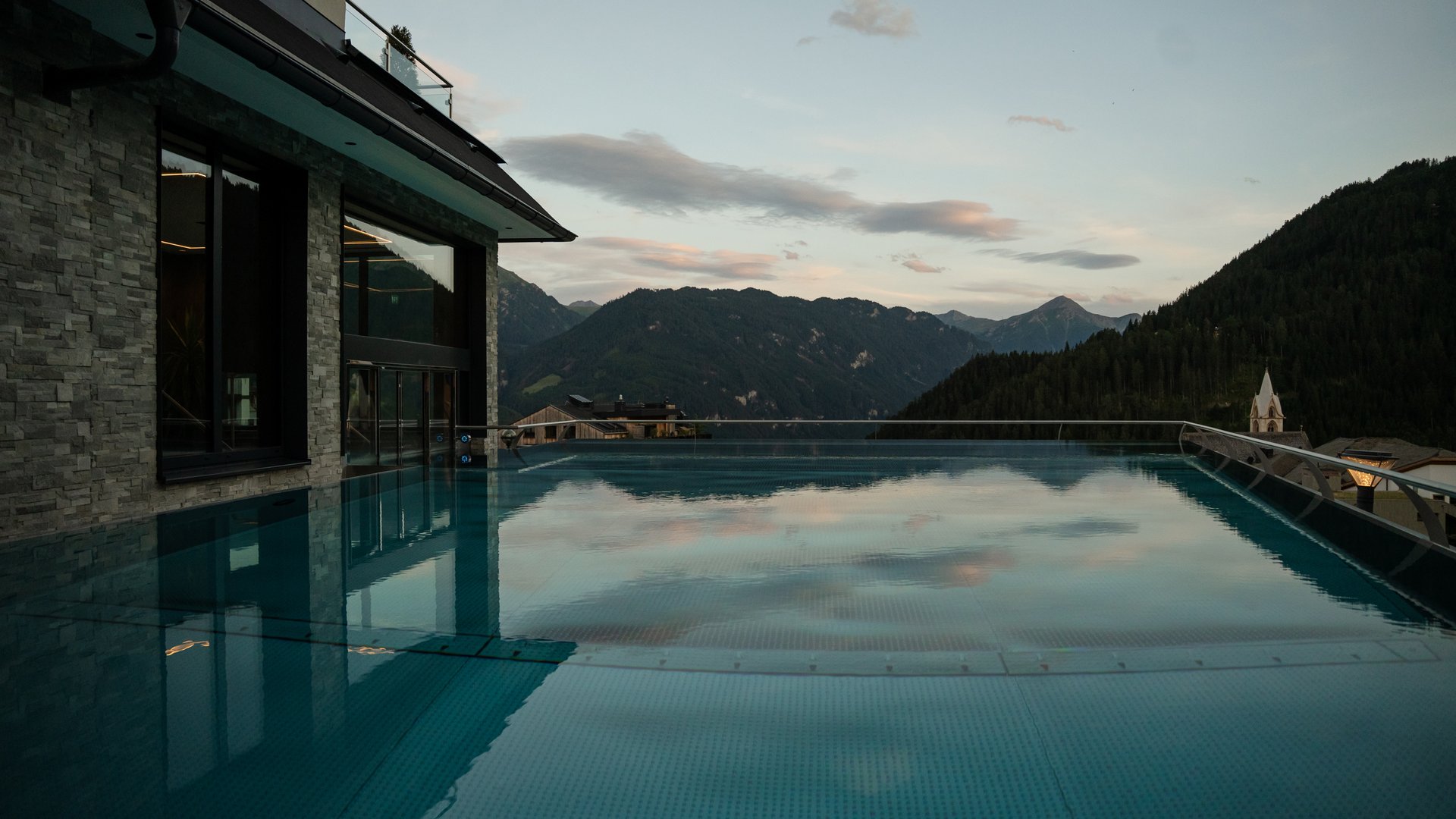 Infinity pool with mountain view and evening sky next to modern building