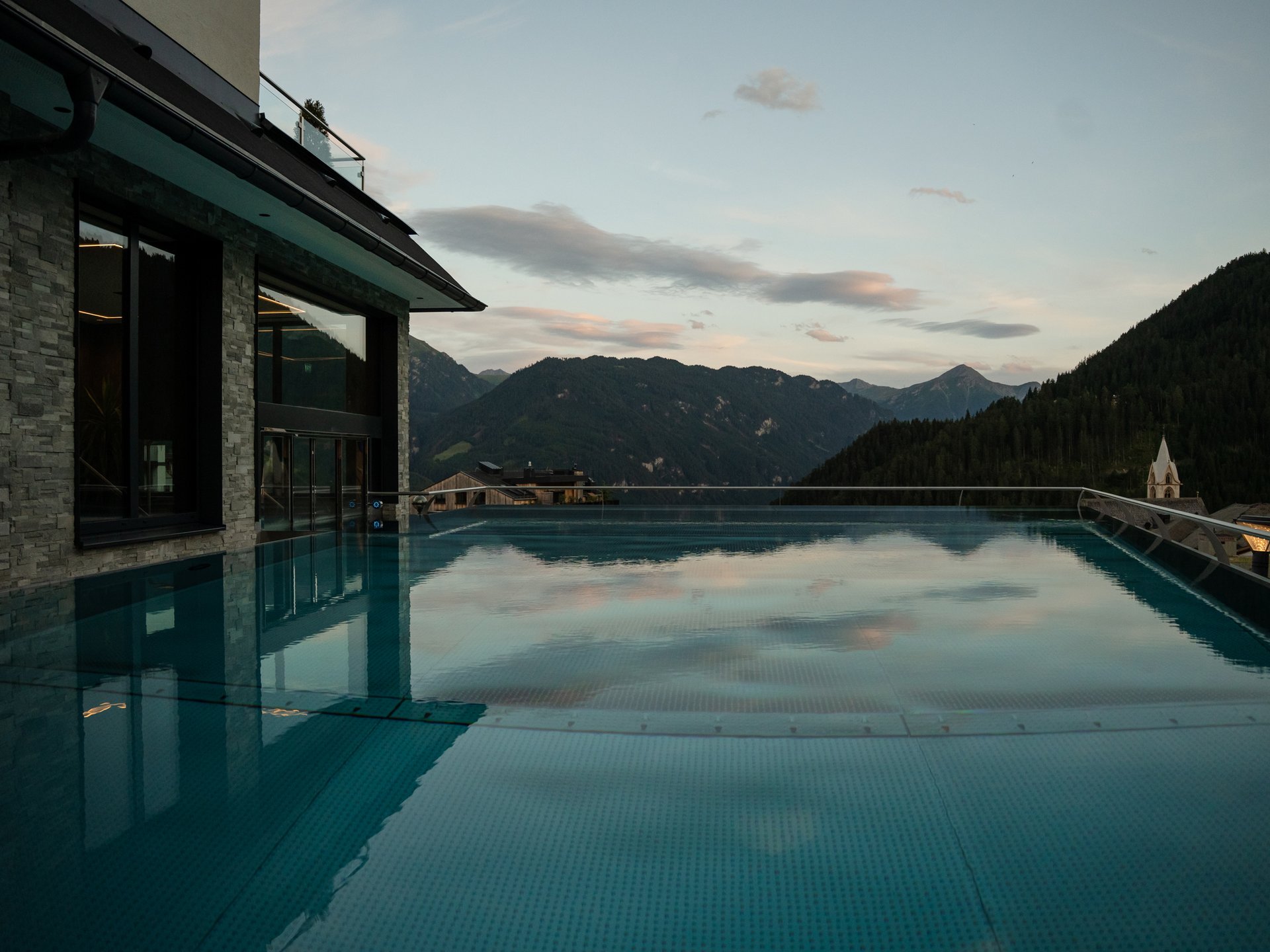 Feel-good holiday at our 5-star hotel in Serfaus Infinity pool with mountain view and evening sky next to modern building