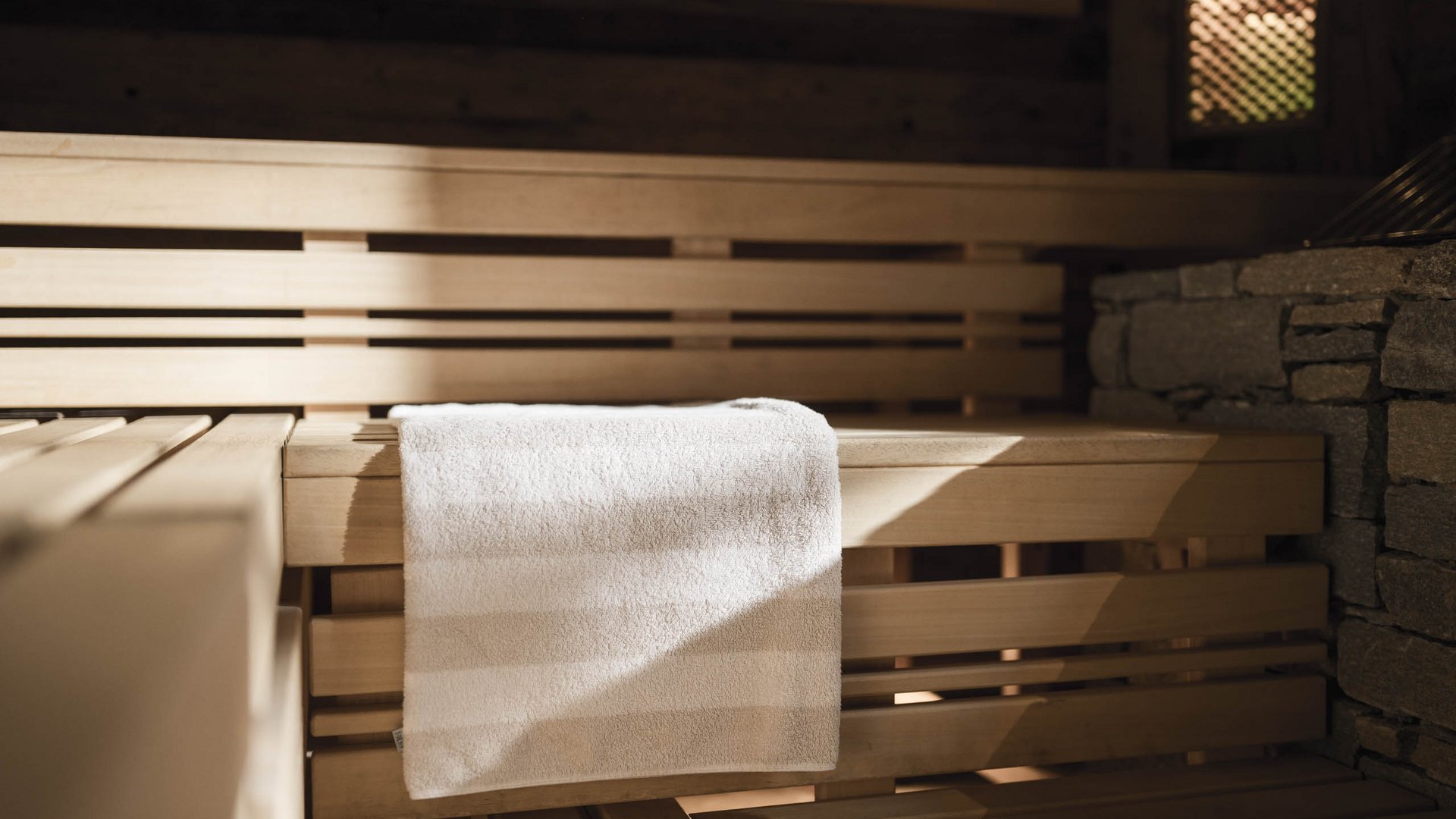 White towel on wooden bench inside a sauna with stone wall