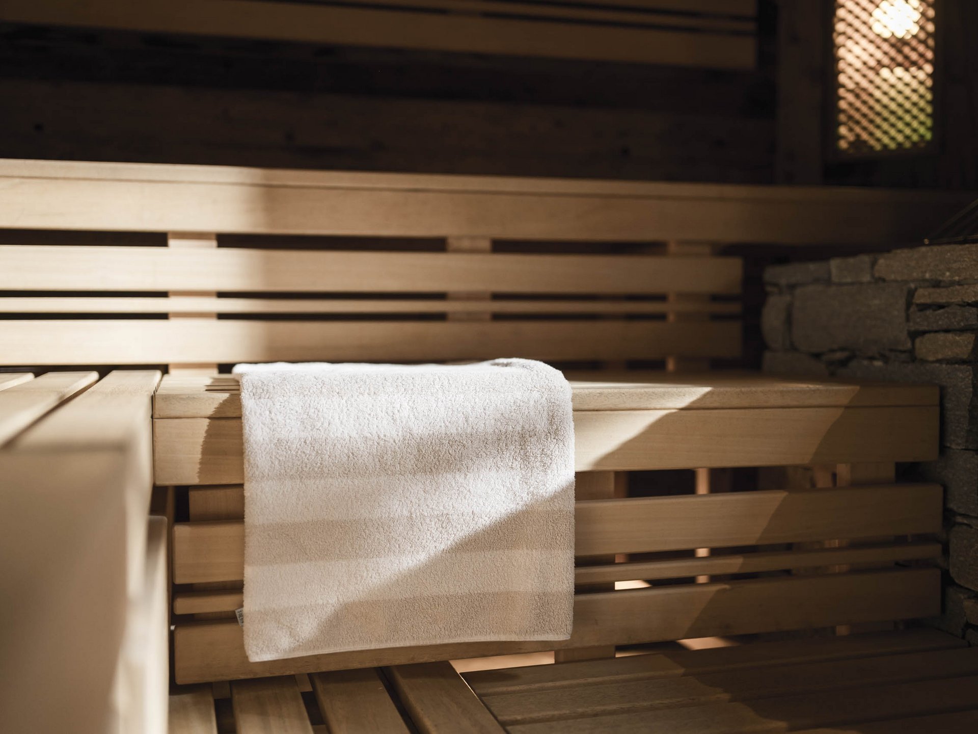 Weißes Handtuch auf Holzbank in einer Sauna mit Steinwand