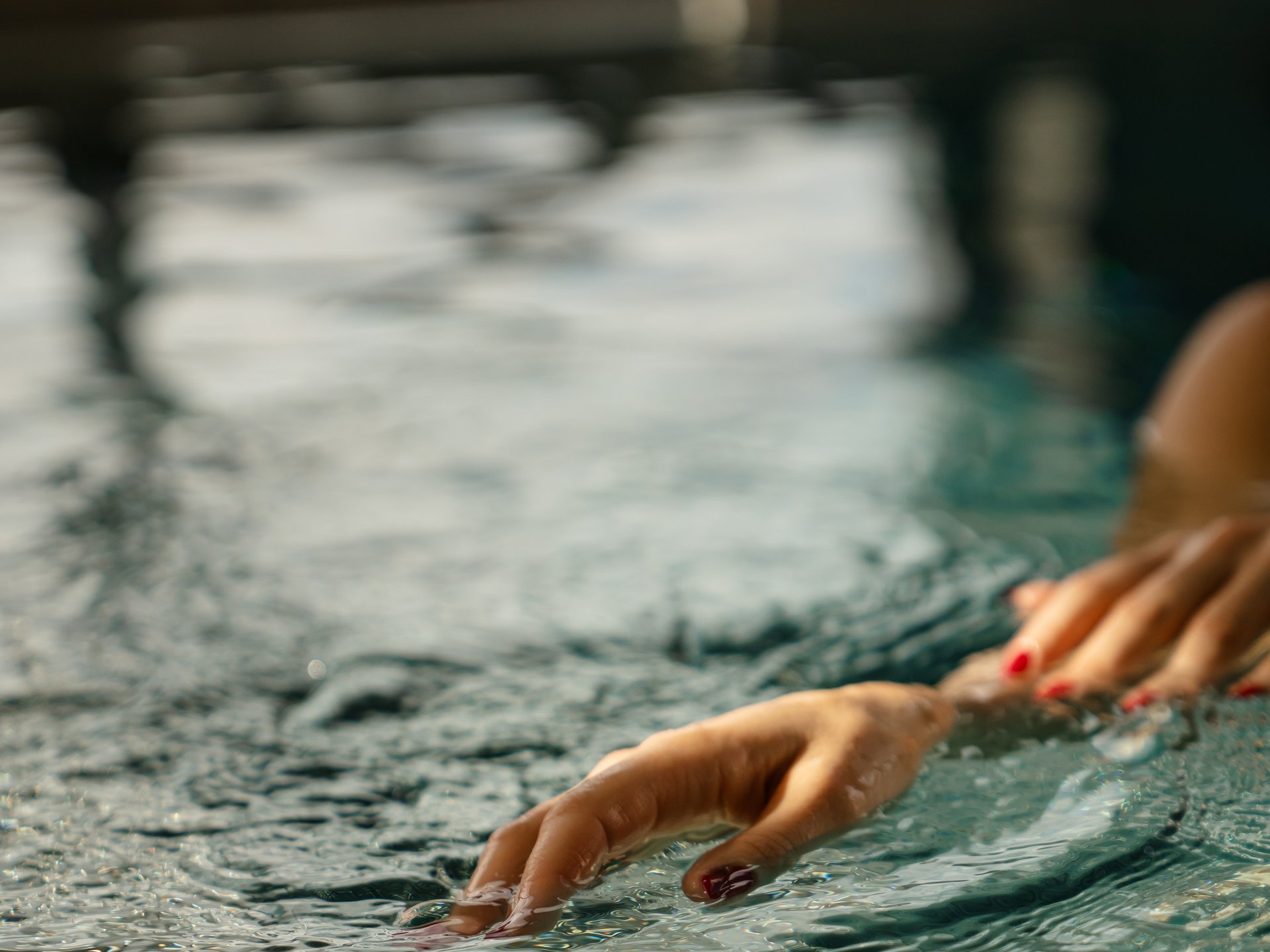 Wohlfühlurlaub im 5-Sterne-Hotel in Serfaus Hand mit roten Fingernägeln berührt Wasseroberfläche im Schwimmbad
