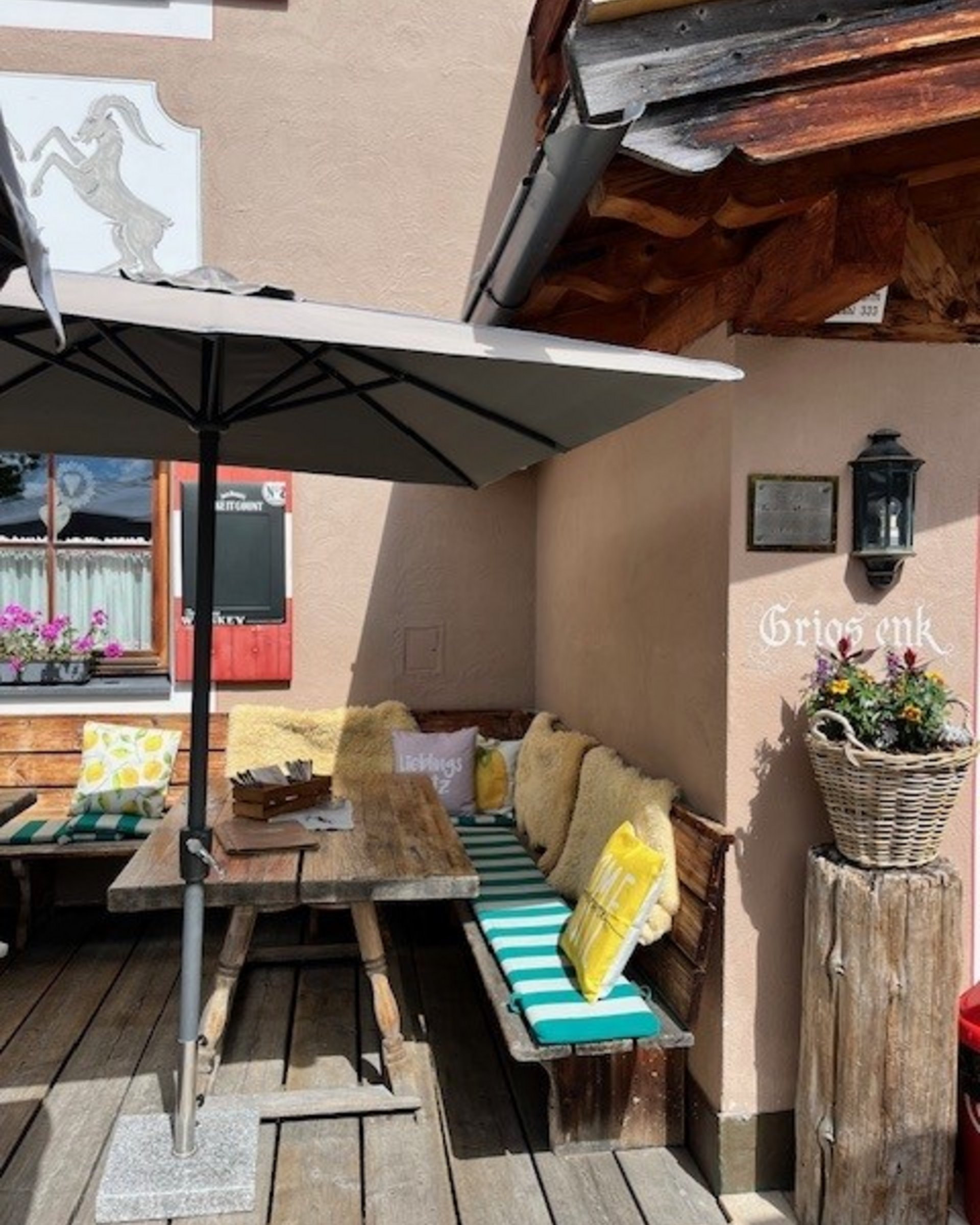 Die Cervosa Alm auf 2 000 Metern Außenbereich mit Holzbänken, Kissen und Sonnenschirm in einem Café.
