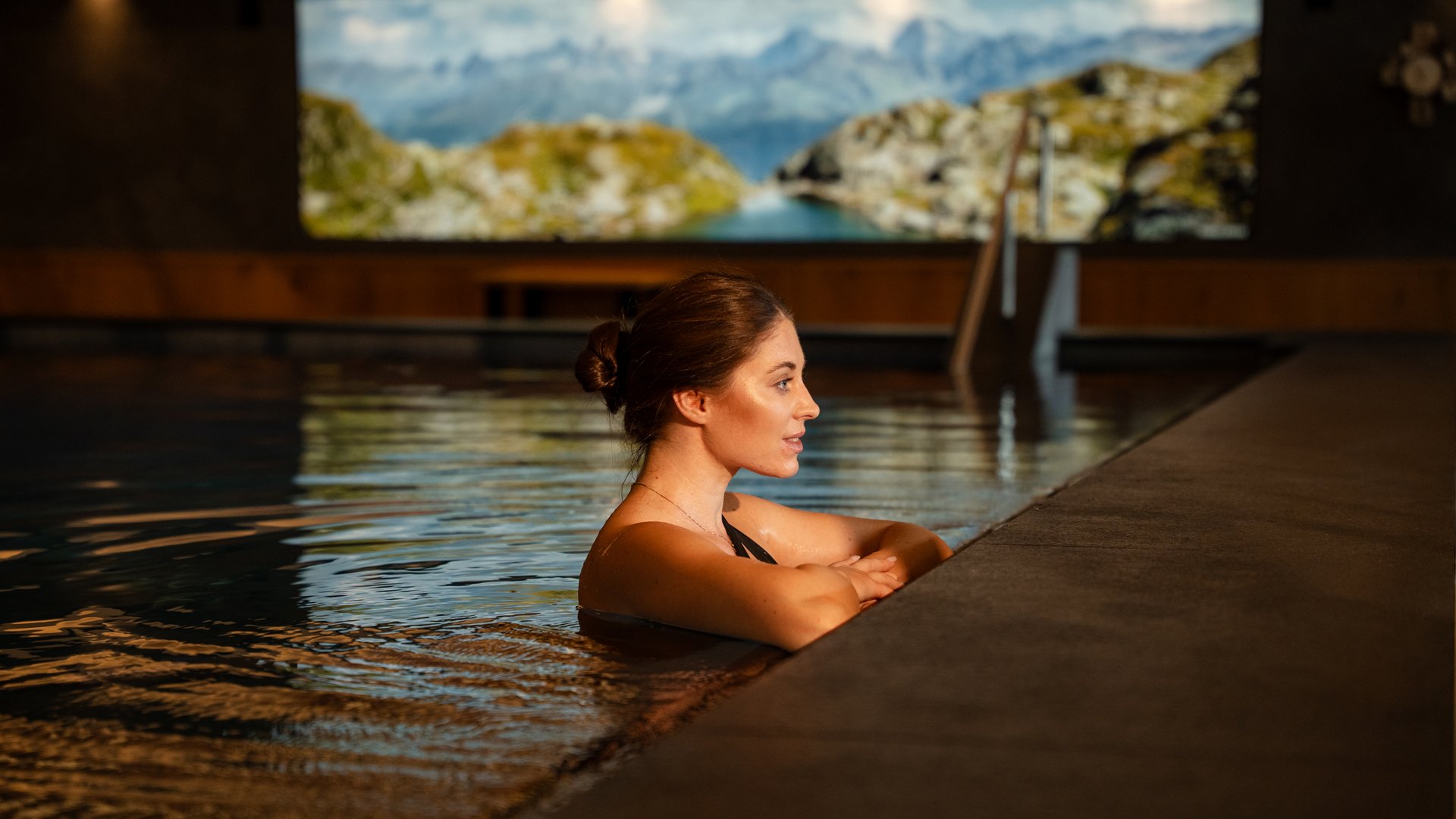 Woman relaxing in indoor pool with mountain landscape in background