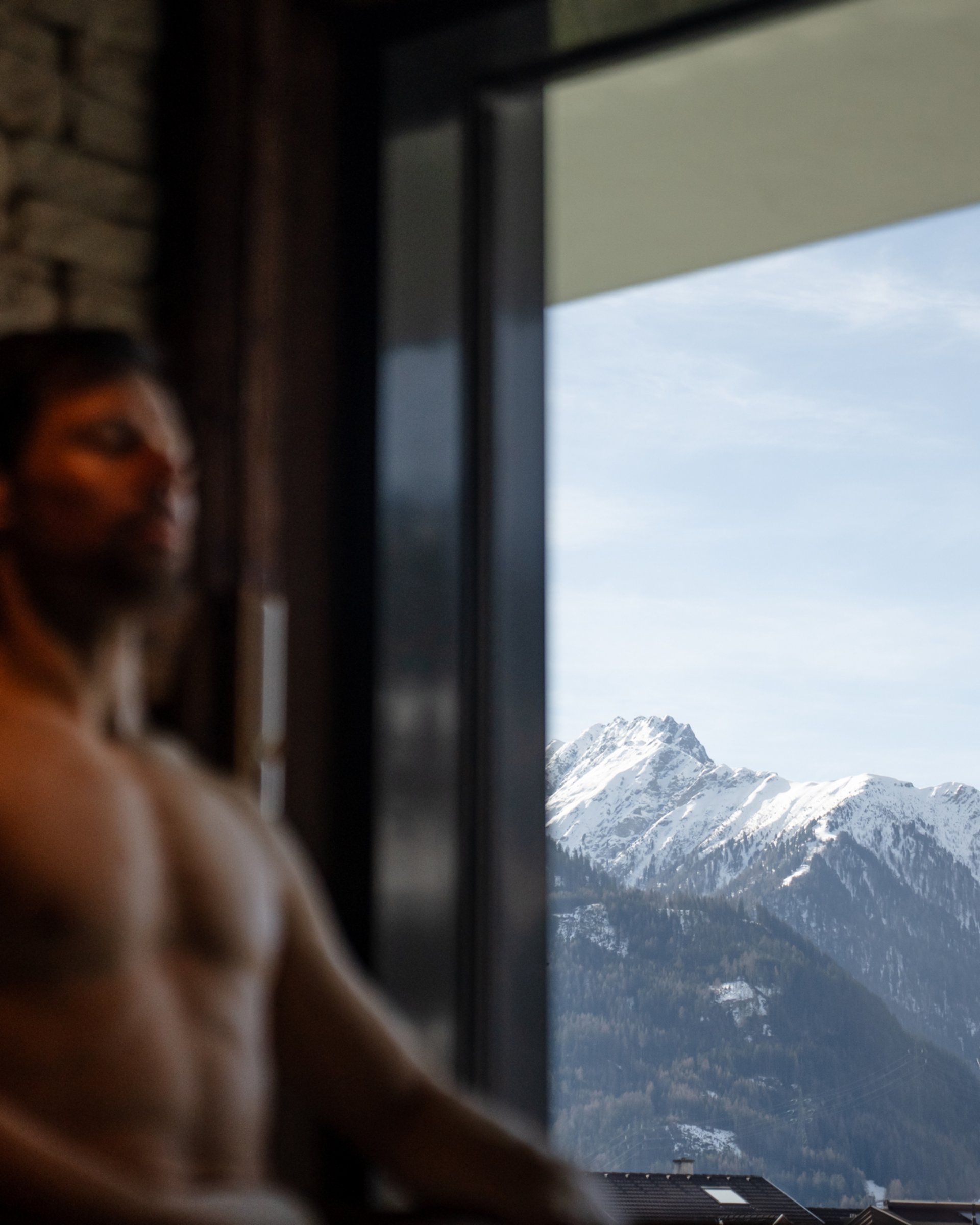 Mann entspannt vor Fenster mit Blick auf schneebedeckte Berge