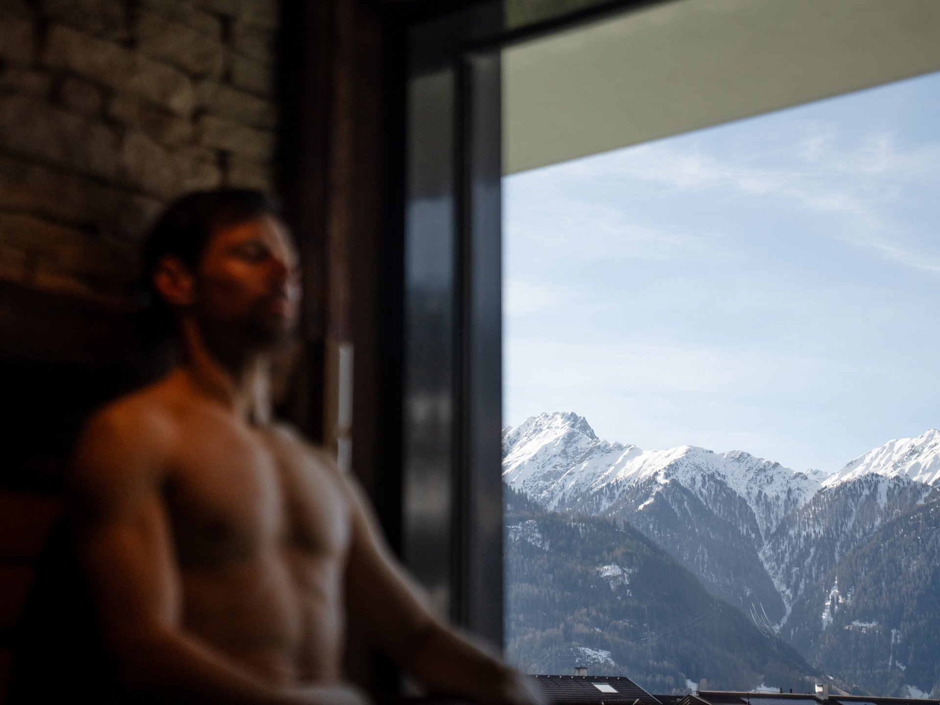Mann entspannt vor Fenster mit Blick auf schneebedeckte Berge