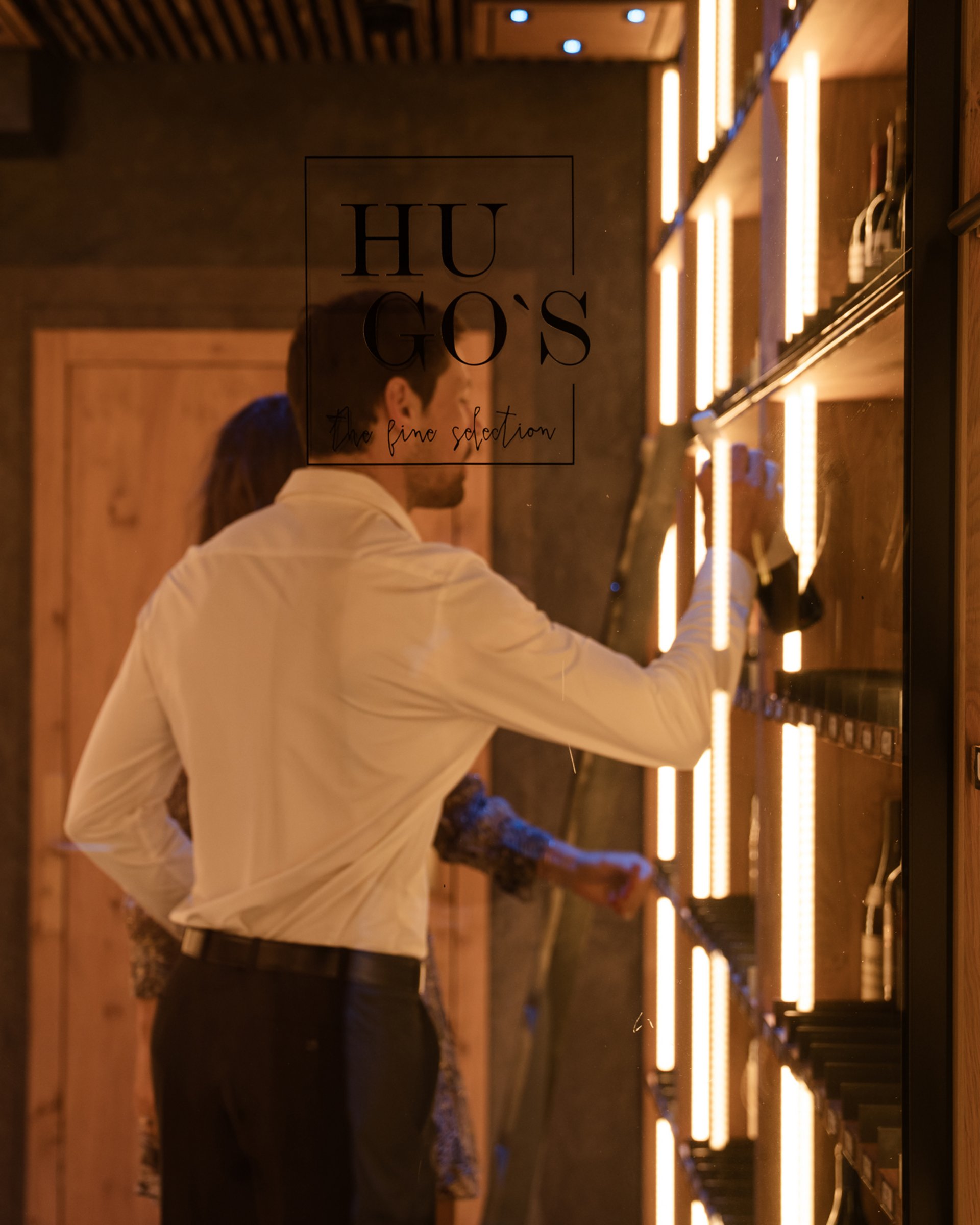 Man selects wine bottle in stylish wooden wine cabinet with warm lighting