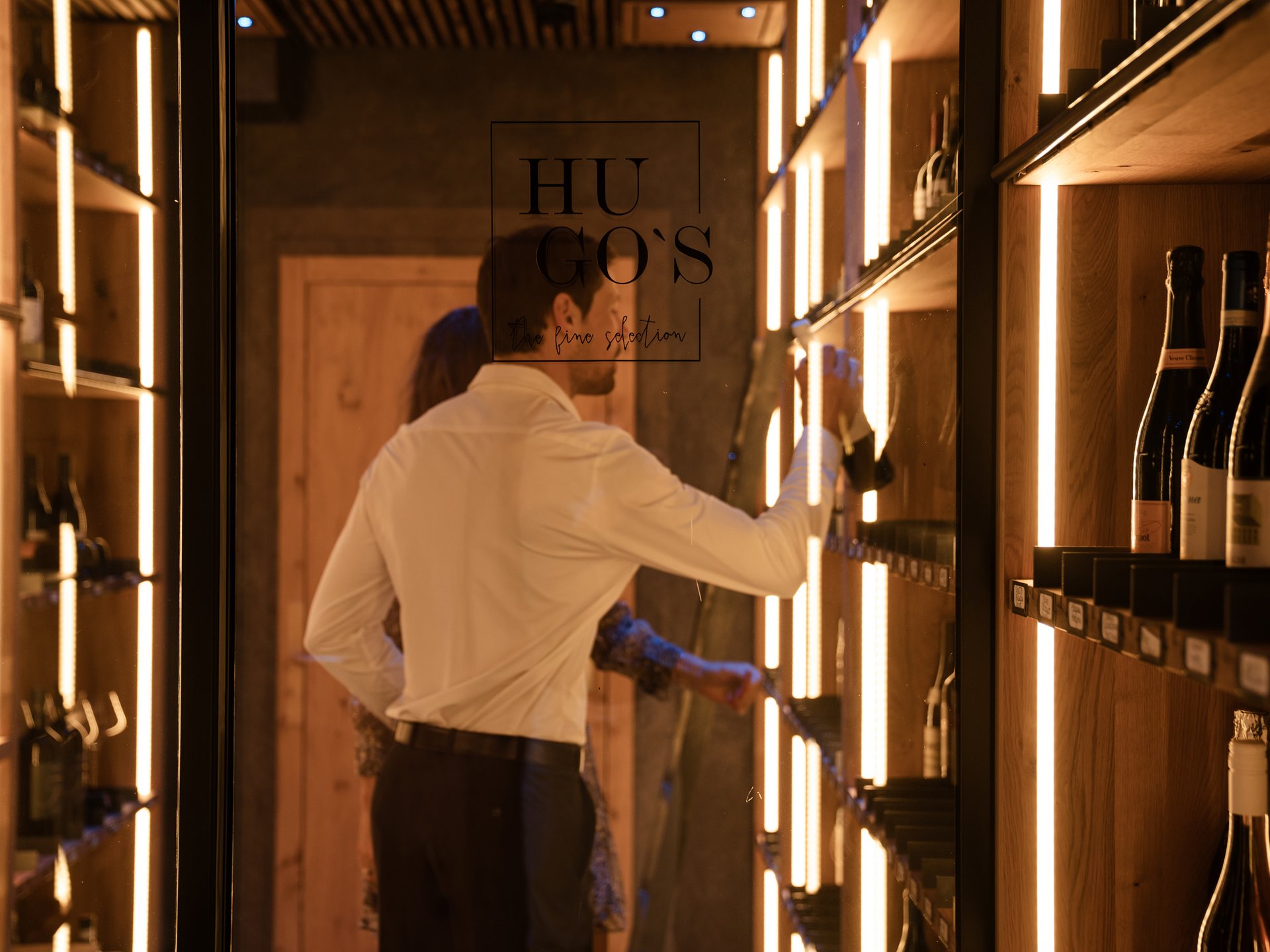 Man selects wine bottle in stylish wooden wine cabinet with warm lighting