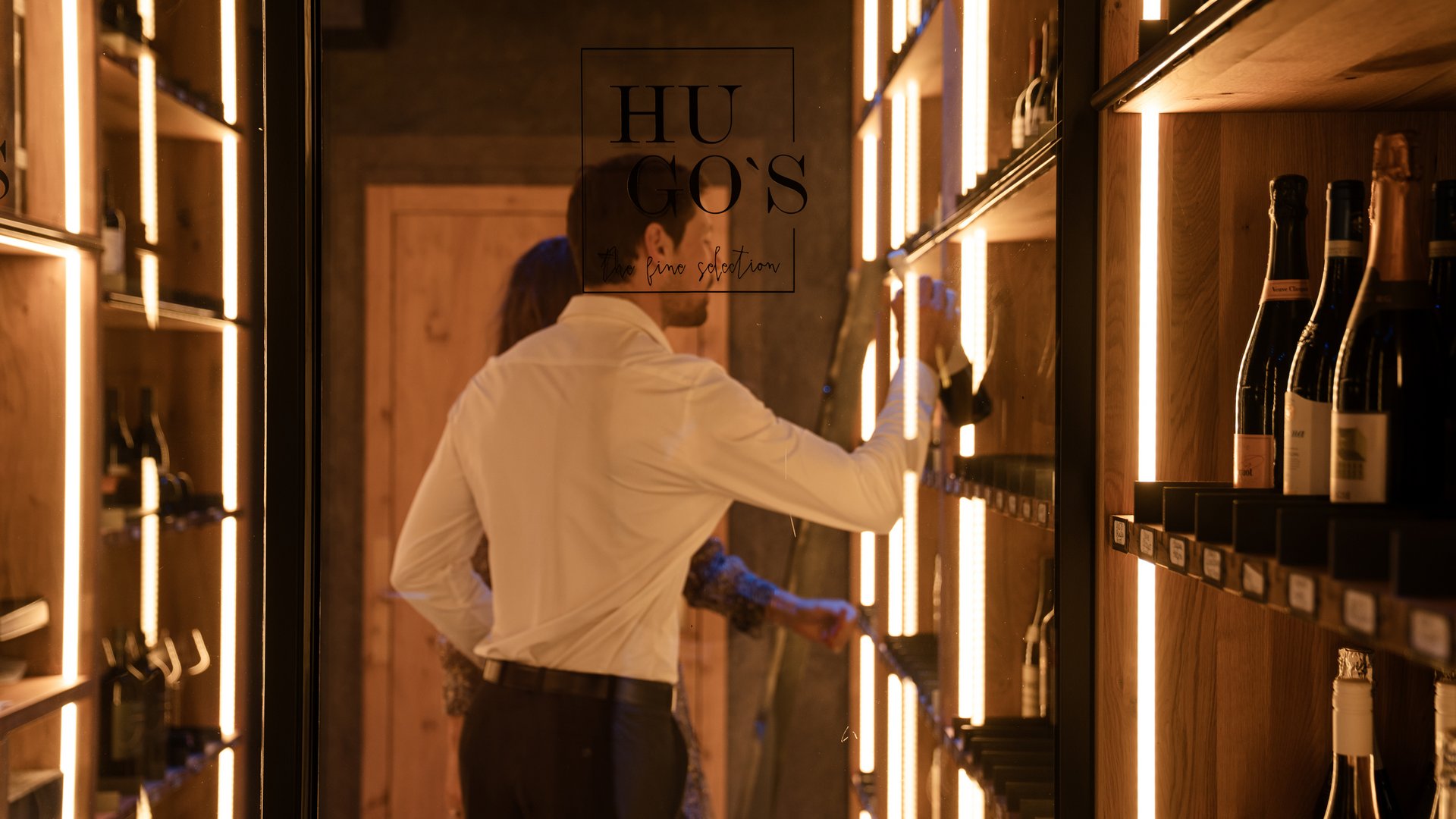Man selects wine bottle in stylish wooden wine cabinet with warm lighting