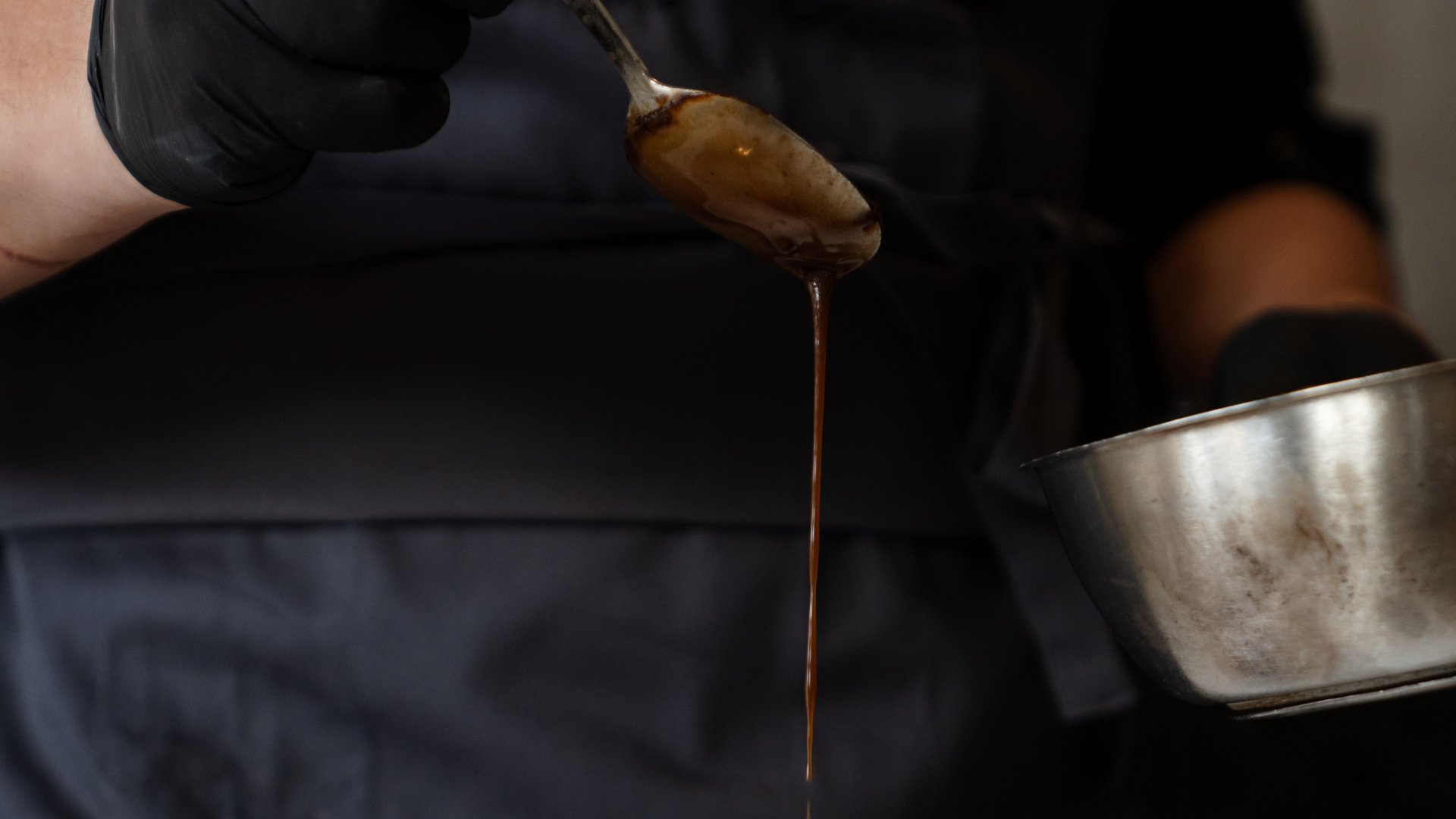 Chef drizzling dark sauce over plated dish in a restaurant