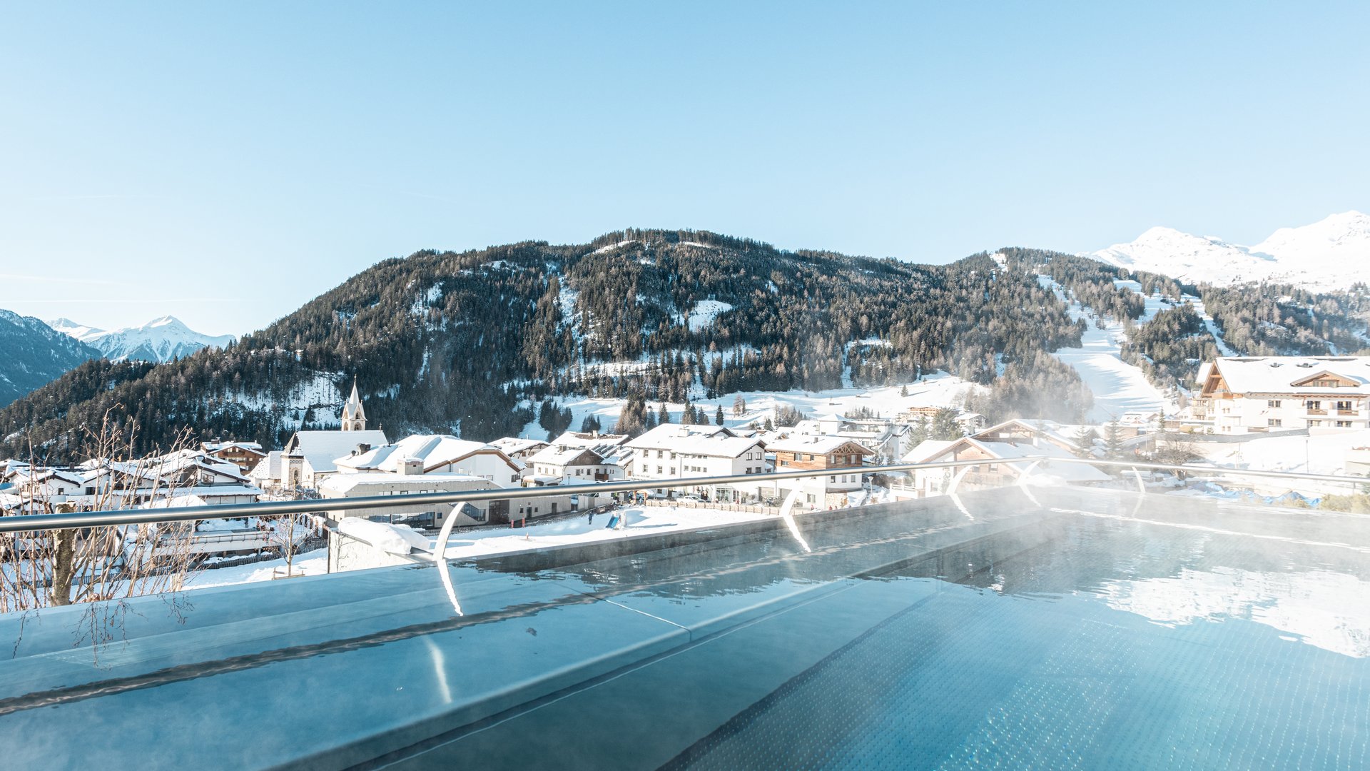 Beheizter Außenpool mit Blick auf schneebedeckte Berge und Dorf im Winter