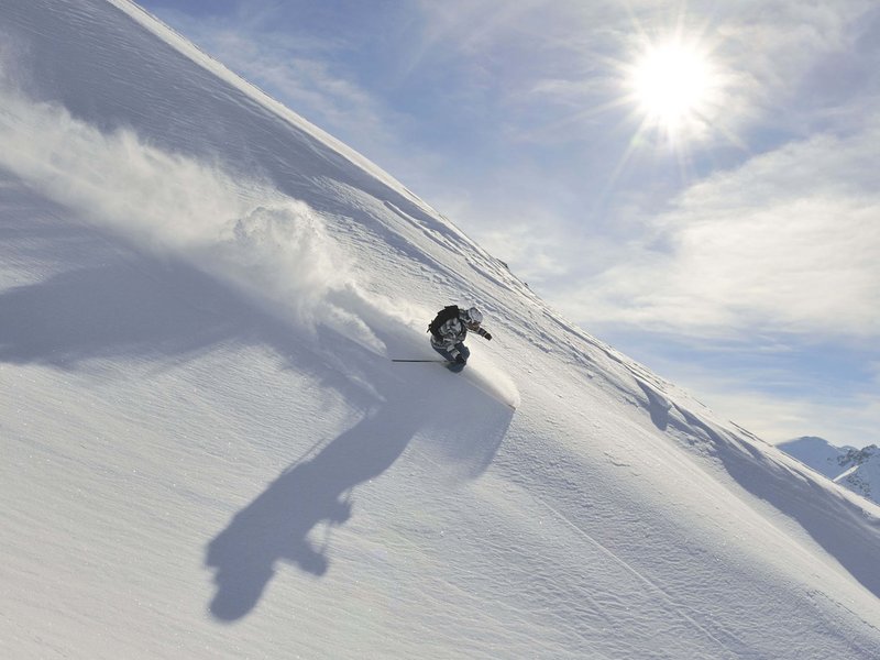 Skifahrer fährt einen verschneiten Hügel bei sonnigem Himmel hinunter