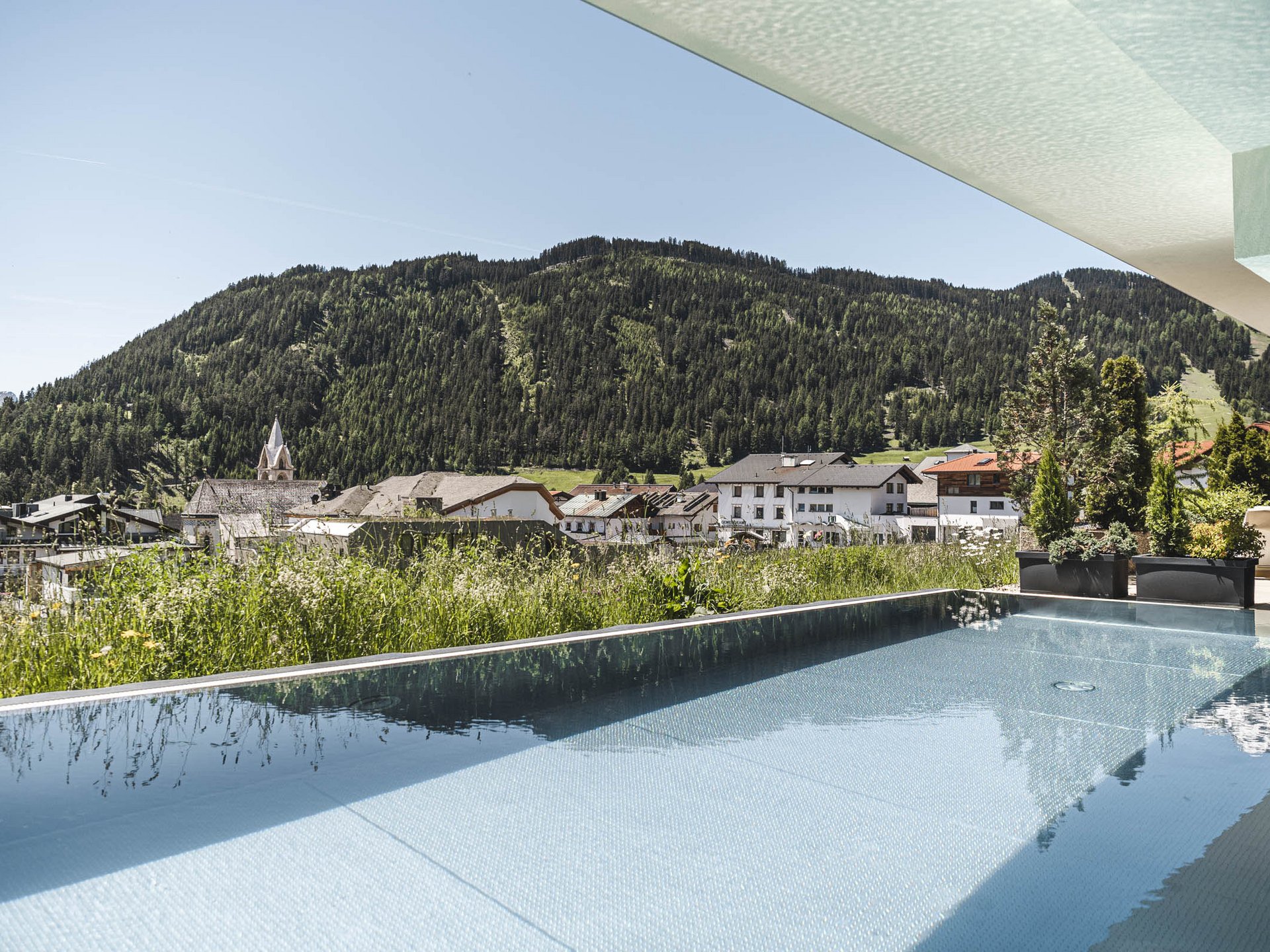 Infinity pool overlooking a mountain village and forest on a sunny day