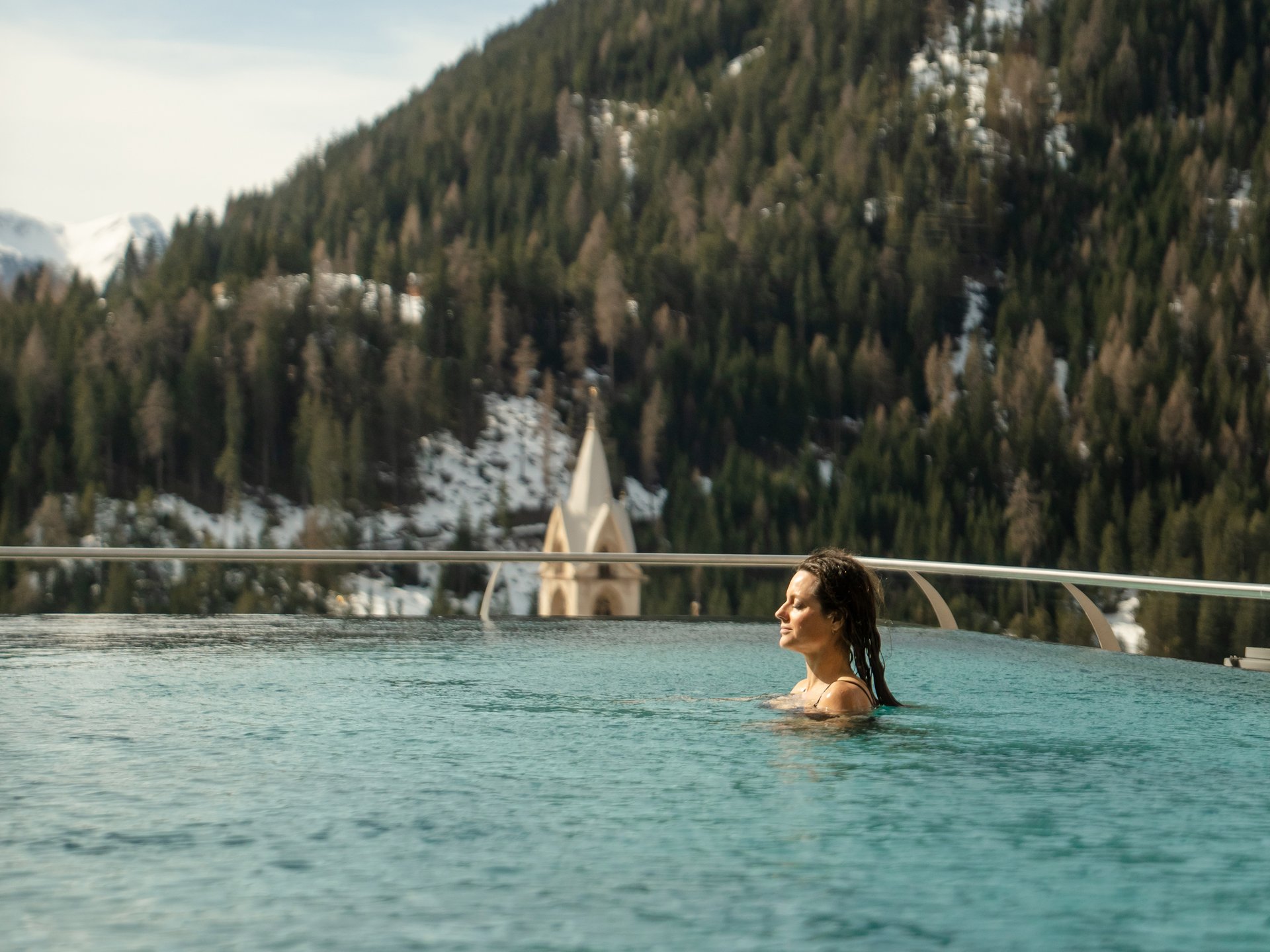 Woman relaxing in pool with mountain landscape and church in background