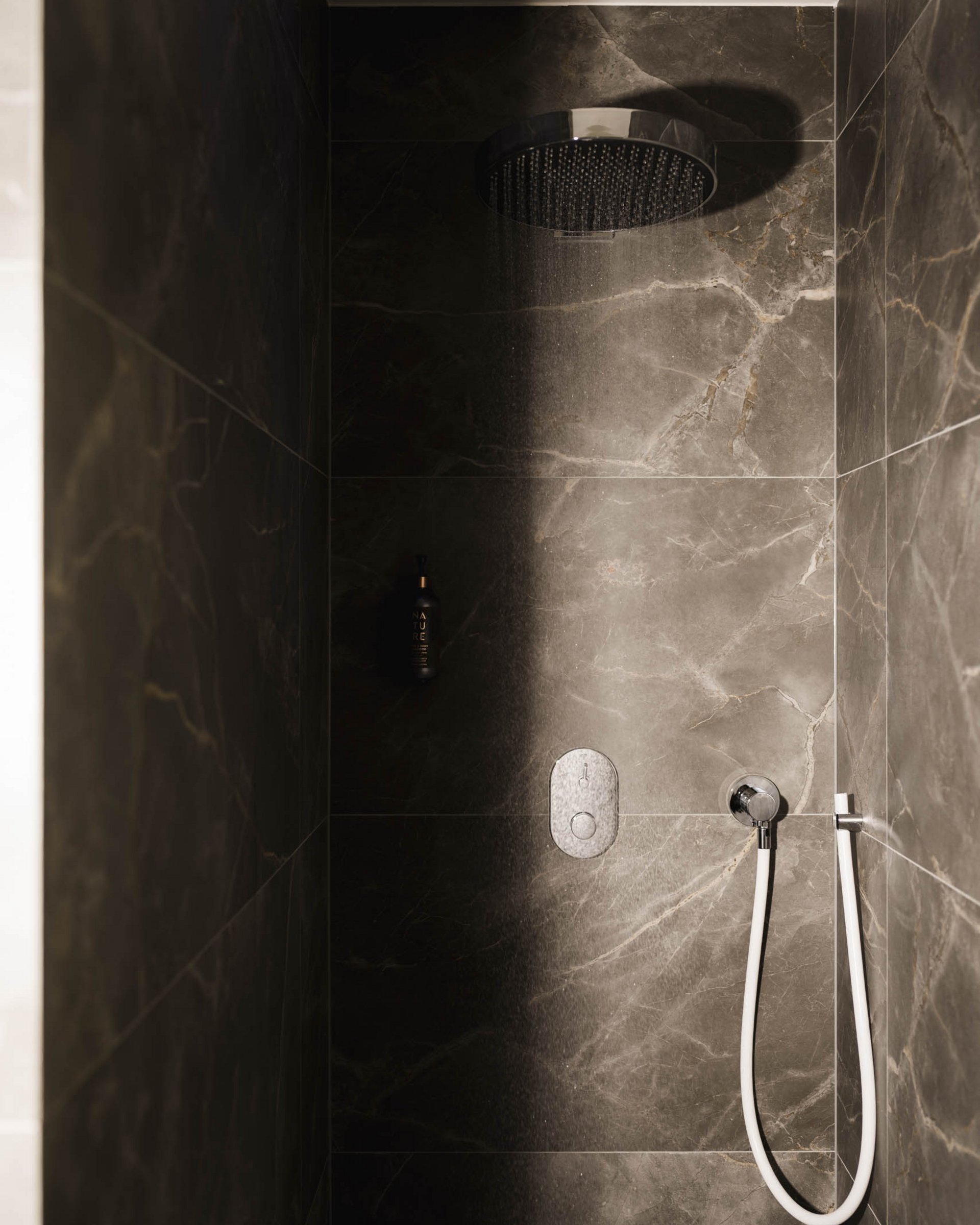 Moderne Dusche mit Regenduschkopf und dunklen Marmorfliesen