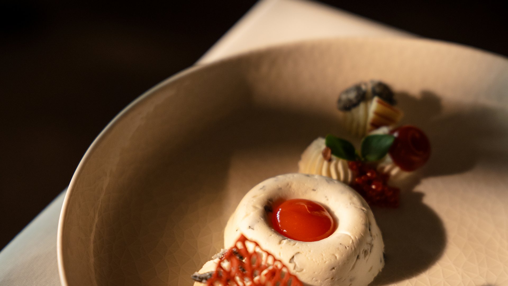 Artfully plated dessert with red sauce and garnishes on beige plate