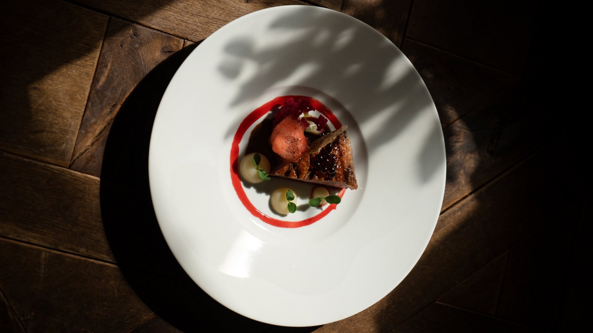 Fein angerichtetes Gourmetgericht auf weißem Teller mit dunklem Holzboden