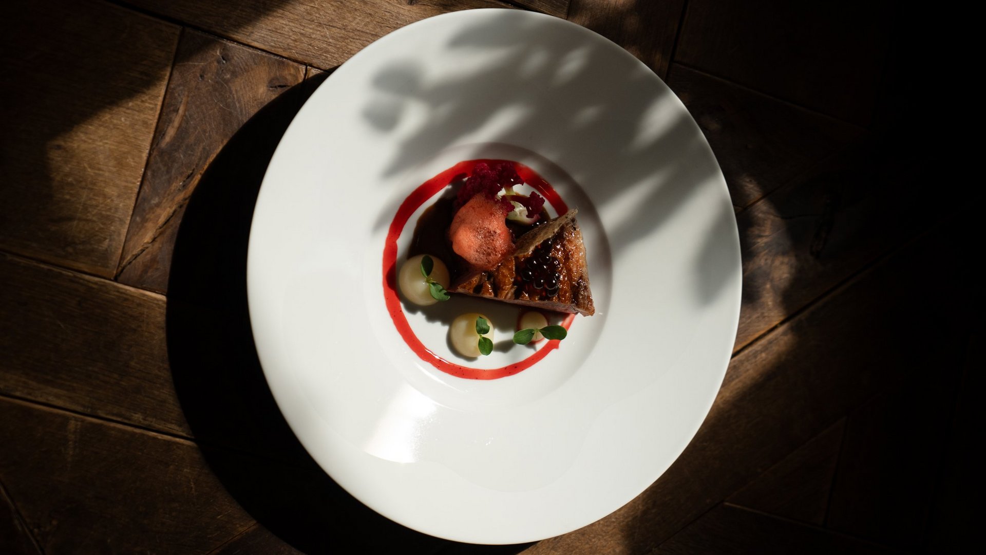 Feel-good holiday at our 5-star hotel in Serfaus Fine dining gourmet dish on white plate with dark wooden floor background