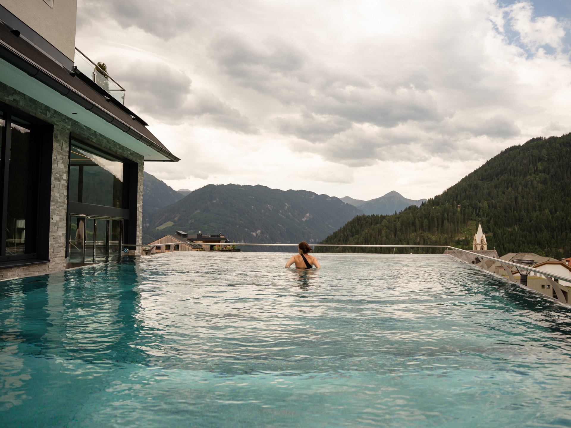 Bathing bliss at our hotel with pool in Serfaus Person swimming in infinity pool with mountain view under cloudy sky