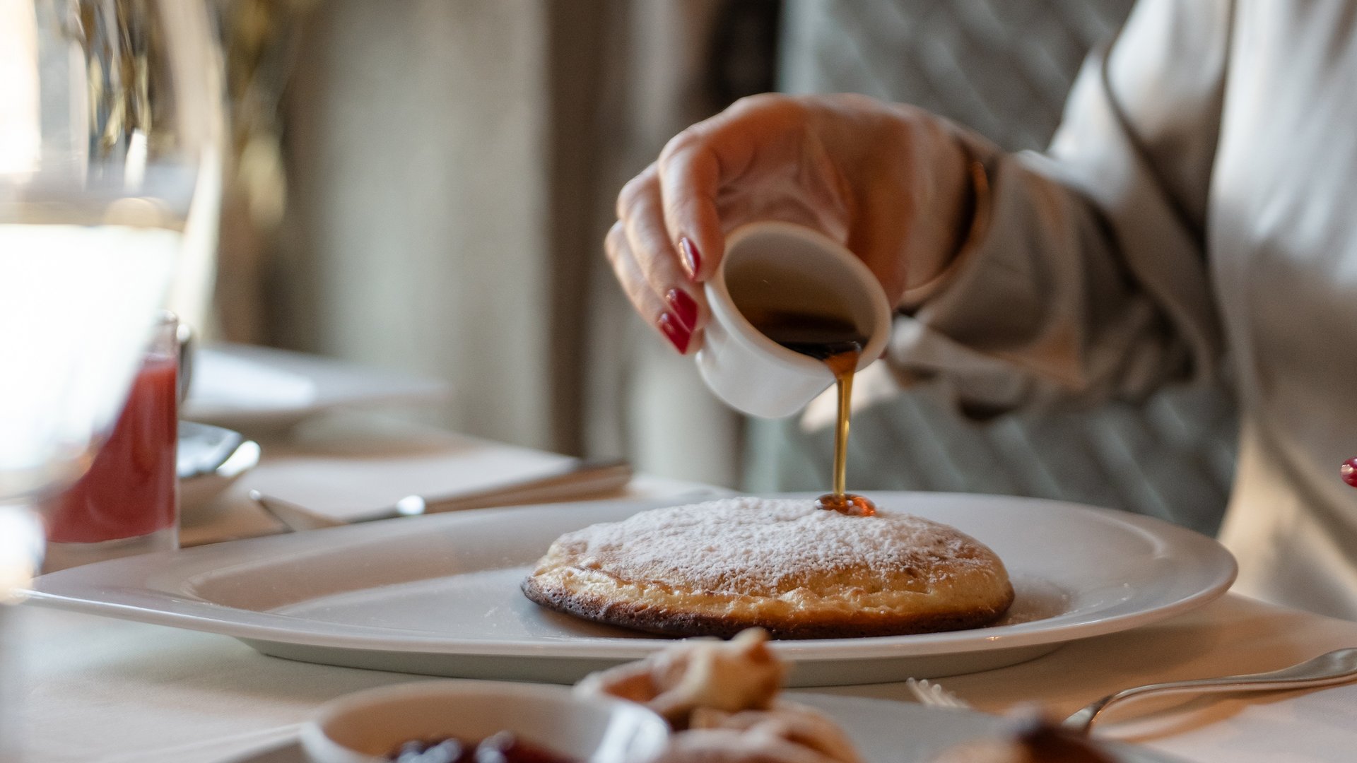Person pouring syrup on a pancake at a set breakfast table