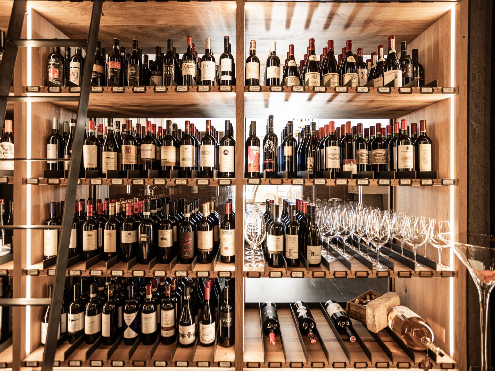 Wine rack with many bottles and glasses on wooden shelves