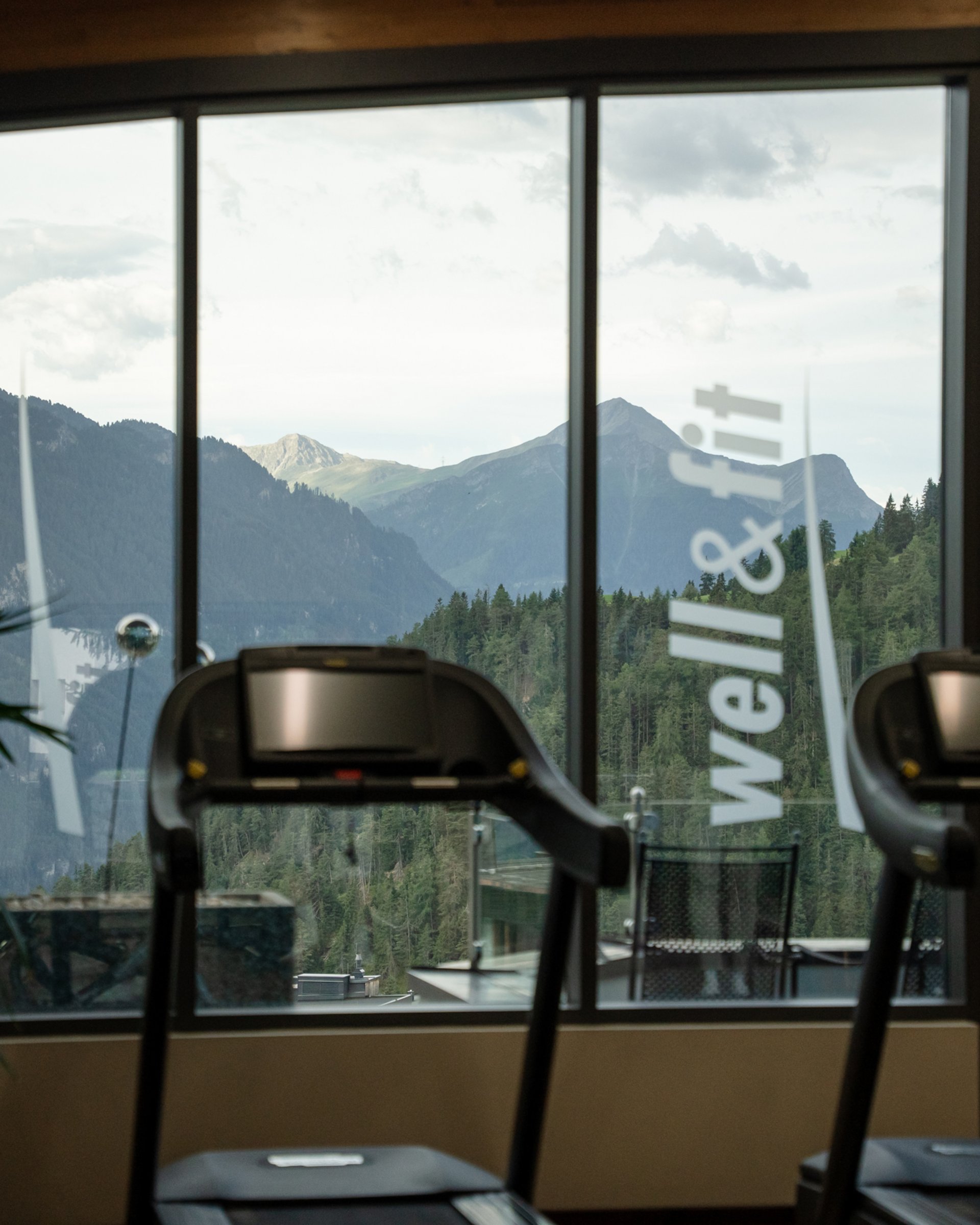 Bewegung im Sporthotel mit Fitnessstudio Fitnessraum mit Laufbändern und Bergblick durch große Fenster