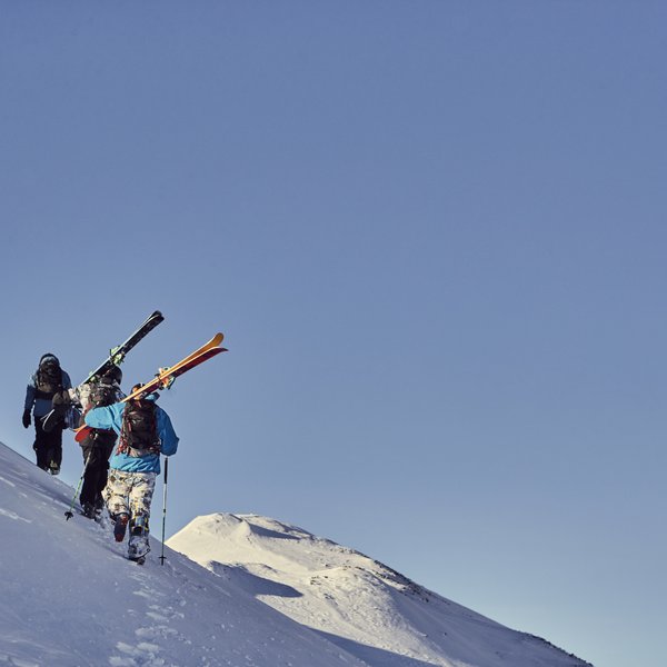 Drei Skifahrer wandern einen schneebedeckten Hang bei klarem Himmel hinauf