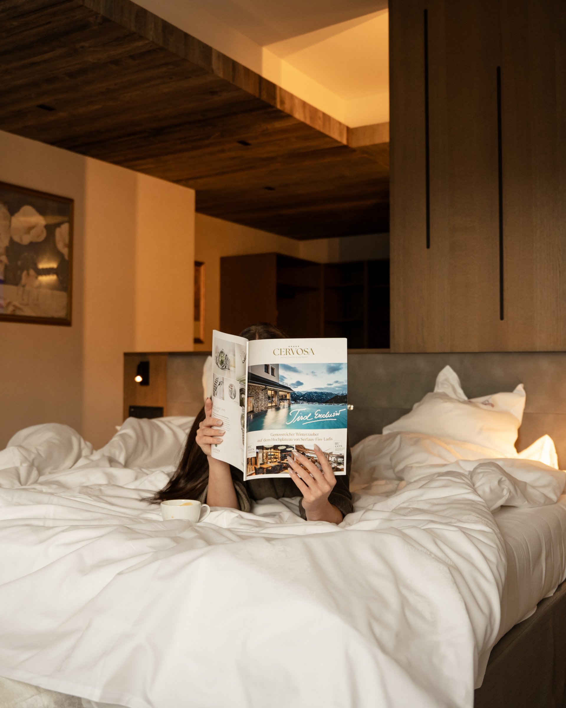 Feel-good holiday at our 5-star hotel in Serfaus Person lying in bed reading a magazine in a cozy hotel room